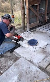 Worker using a power saw to cut concrete near a barn entrance, with white dust covering the floor