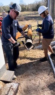 Two workers in hard hats lifting a large pipe on a construction site