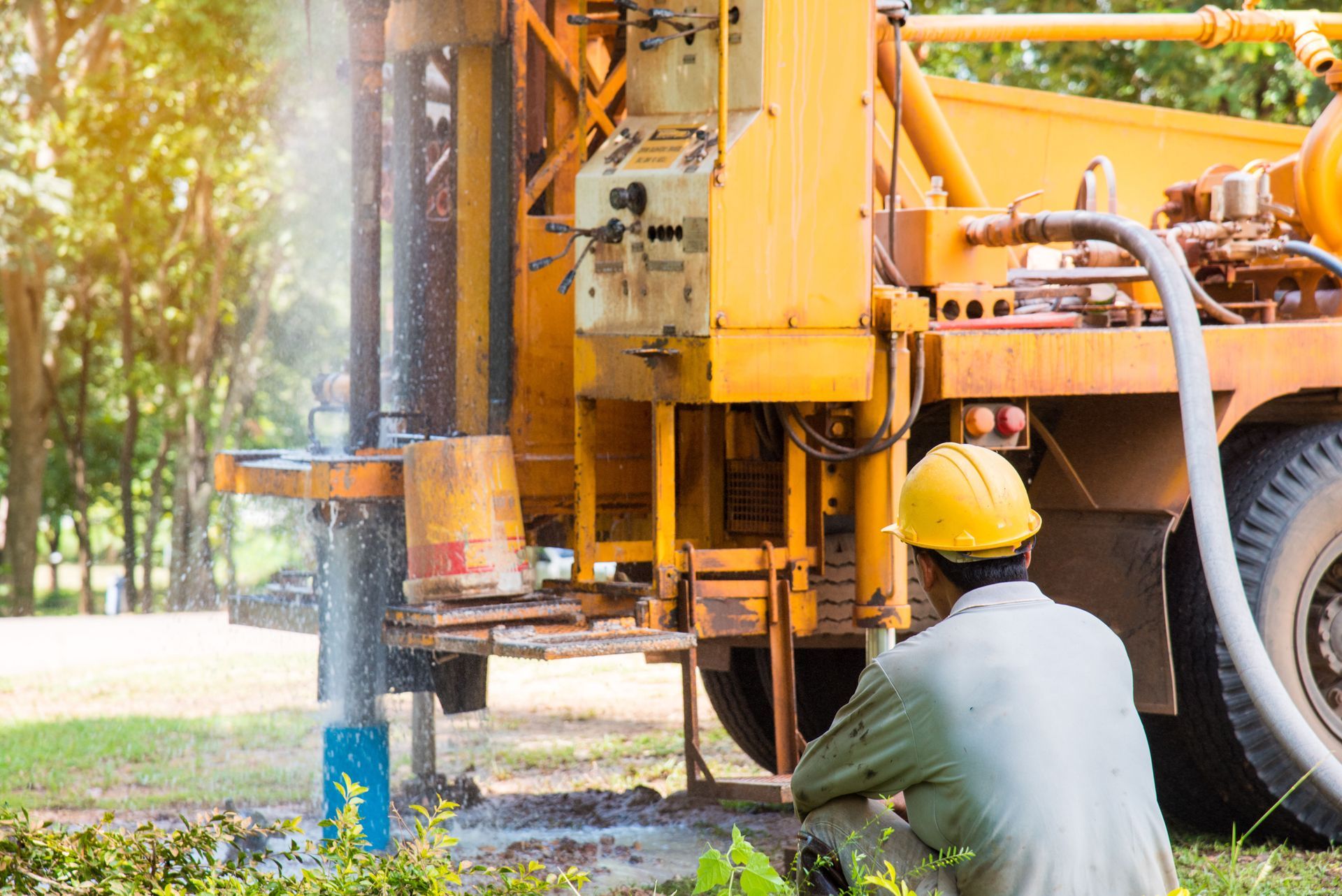 Worker in hard hat operating orange drilling truck at an outdoor construction site
