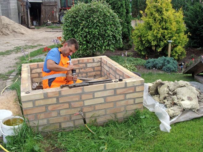 Worker in orange safety vest laying bricks around a small square structure