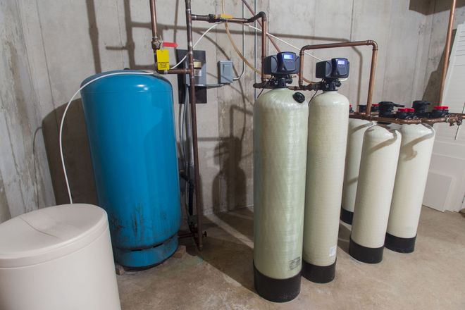 Water treatment equipment with blue and white tanks, pipes, and filters in a basement utility room