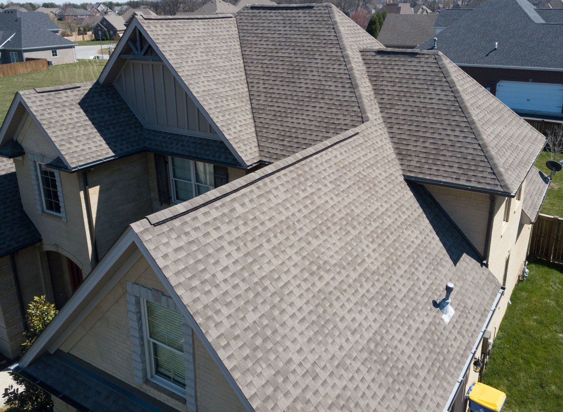 Aerial view of a house with multiple gray shingled roofs and beige siding.