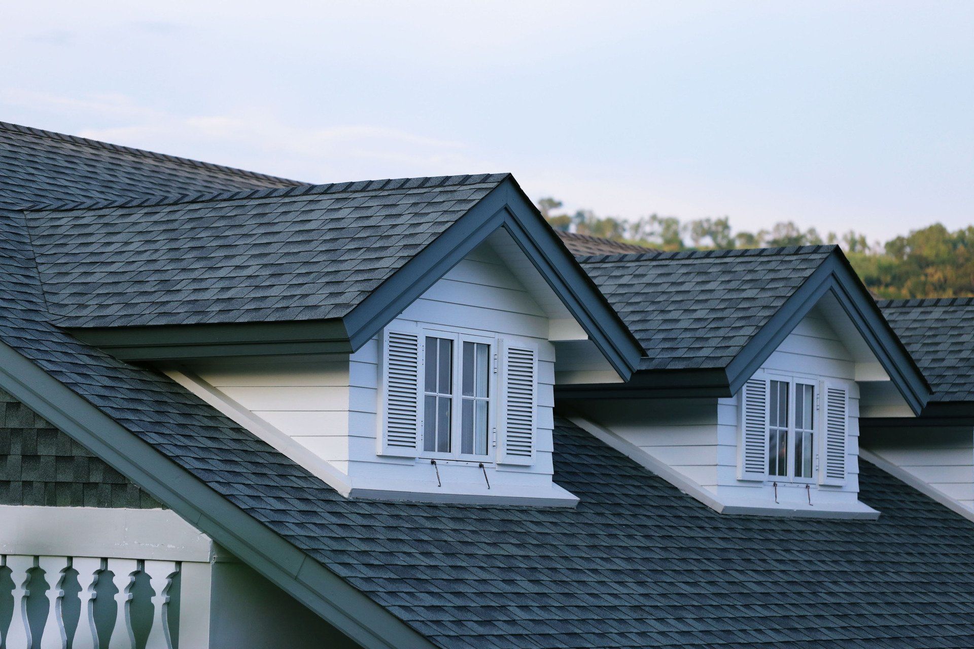 Blue shingled house roof with two dormer windows at dusk.