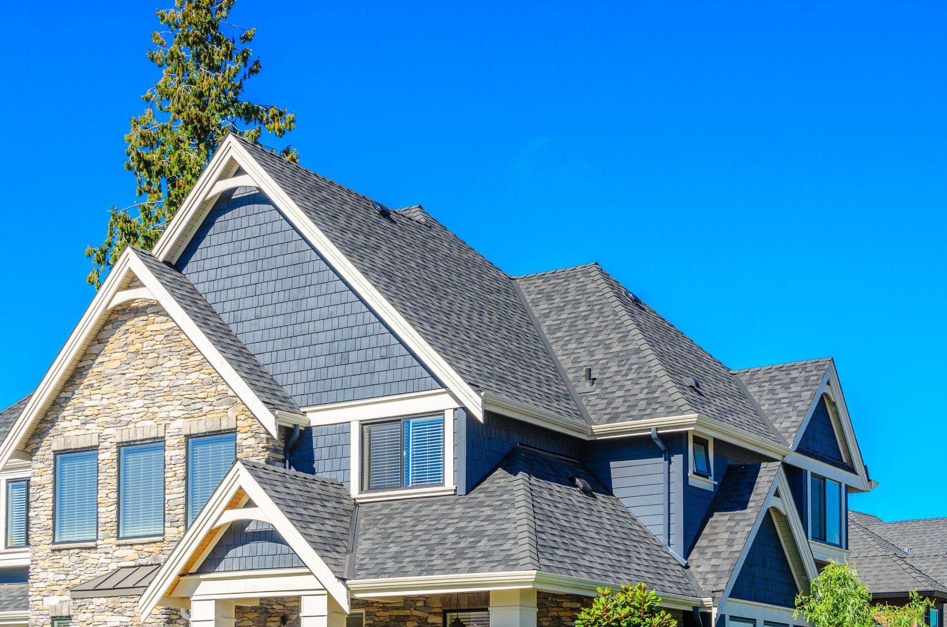Blue-roofed suburban house with stone and wood siding under a bright blue sky.