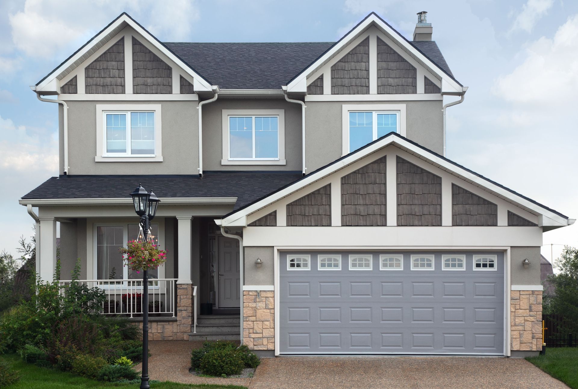 Suburban two-story gray house with a double garage and stone accents under a cloudy sky.