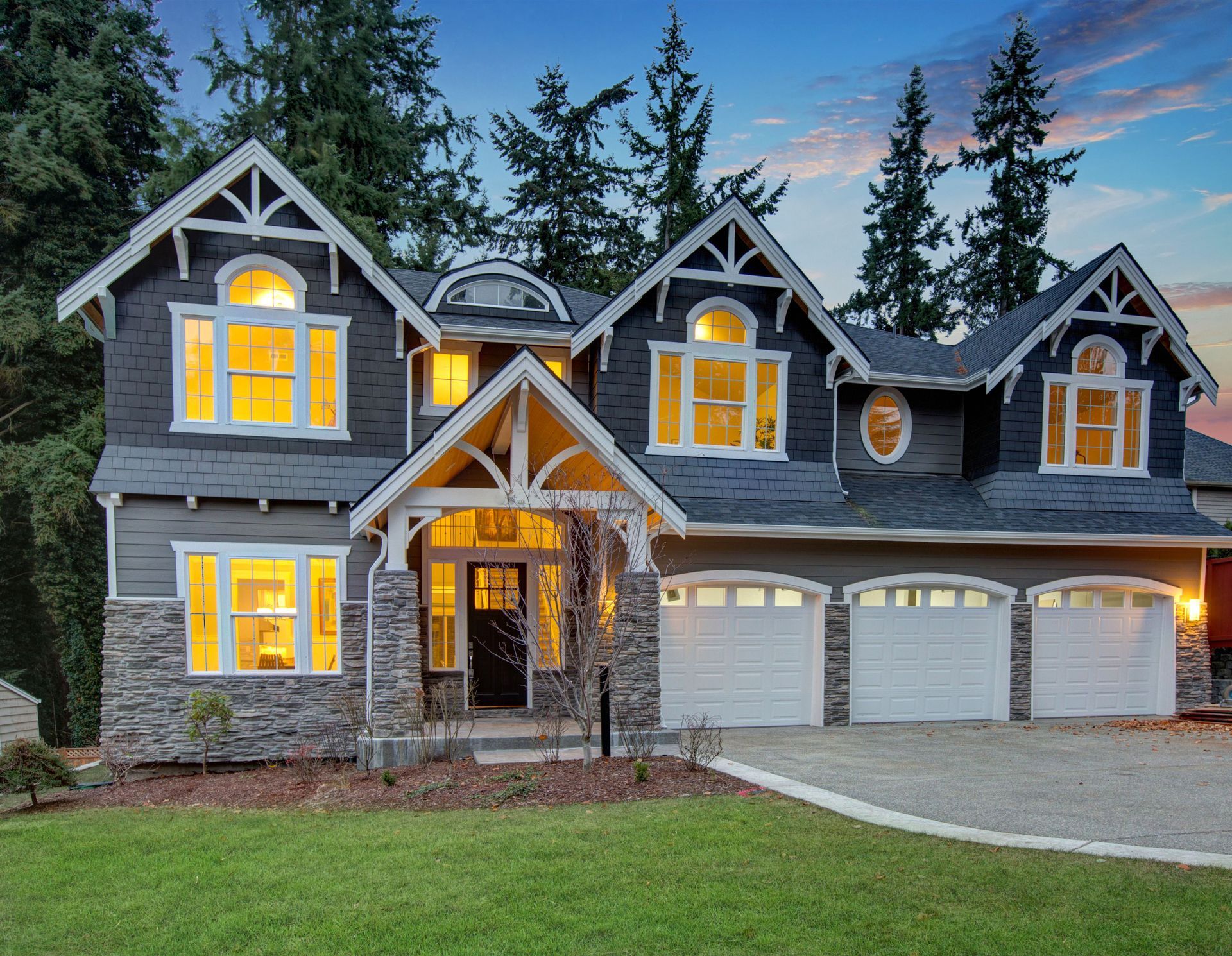 Gray two-story house with lit windows, white trim, and a three-car garage at dusk.