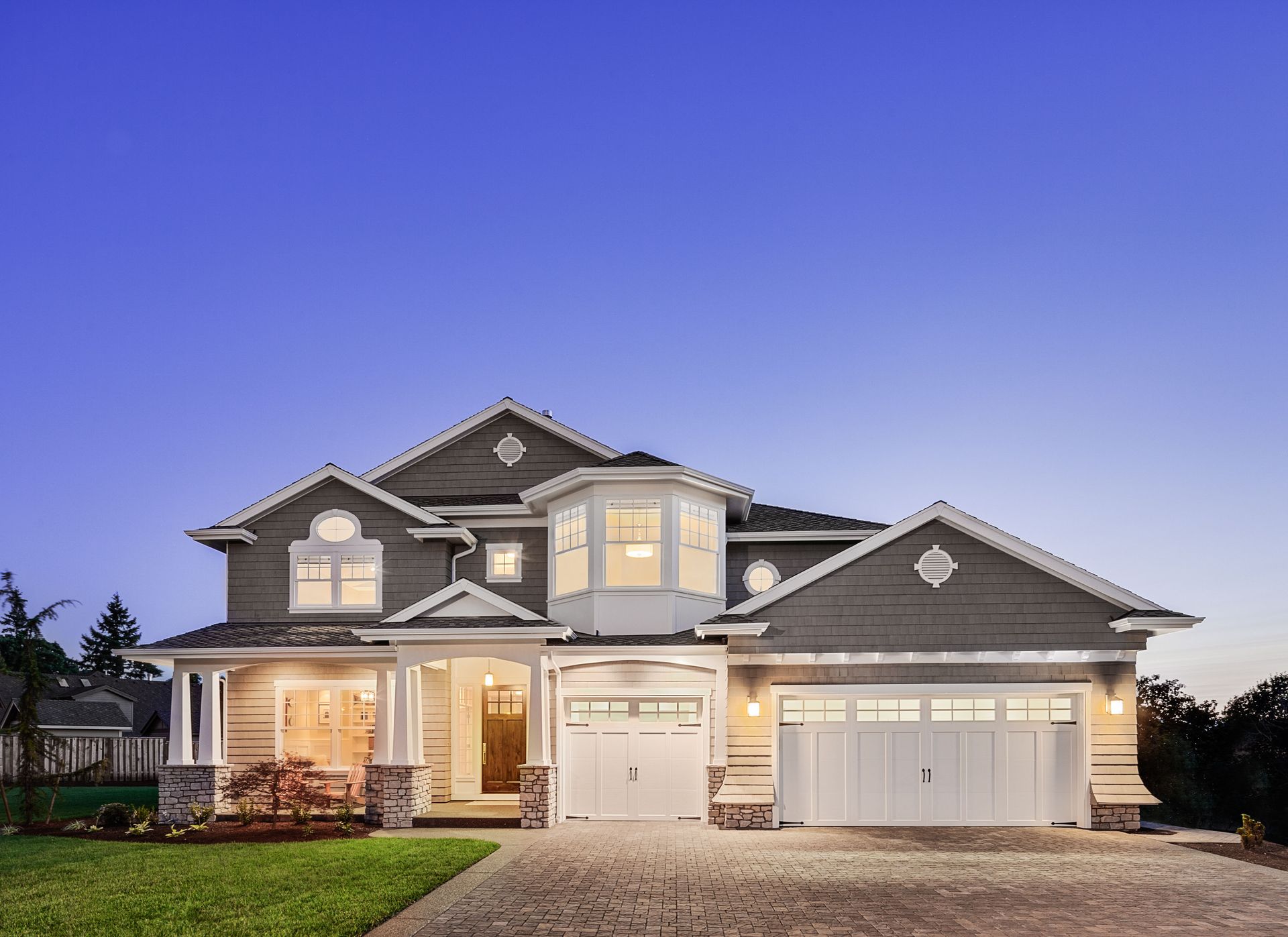Large two-story suburban house with lit windows, white trim, and a three-car garage at dusk.