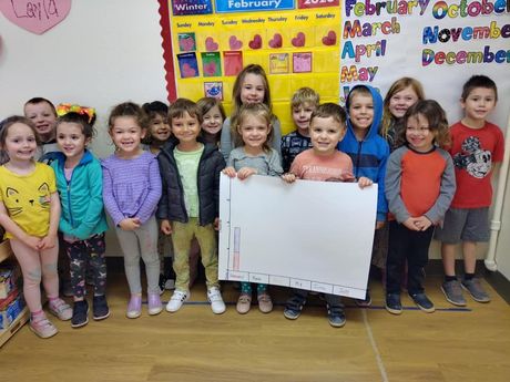 A group of children are posing for a picture in front of a calendar.