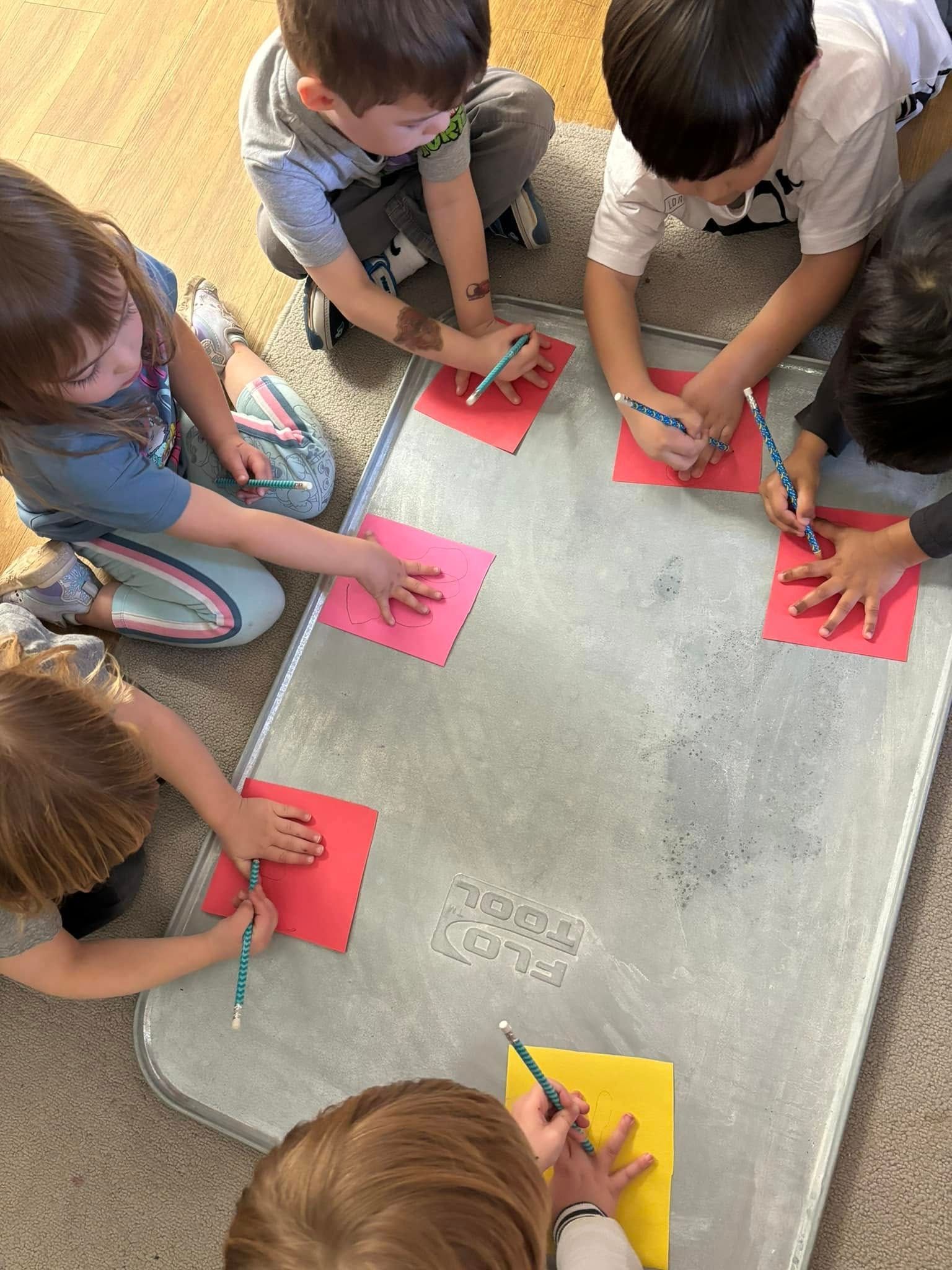 A group of children are sitting around a table writing on paper.