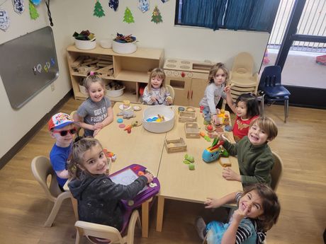 A group of children are sitting around a table in a classroom.