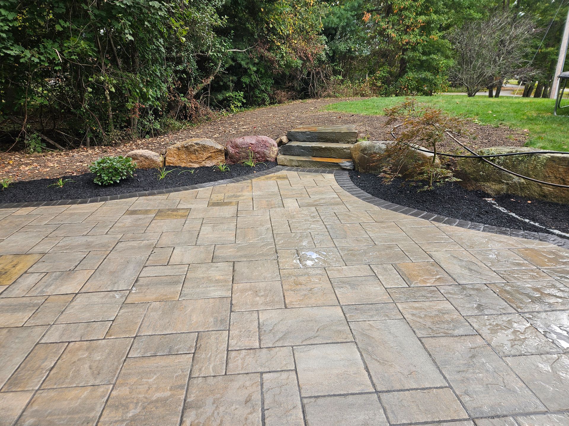 A brick patio with stairs leading up to it in a backyard.