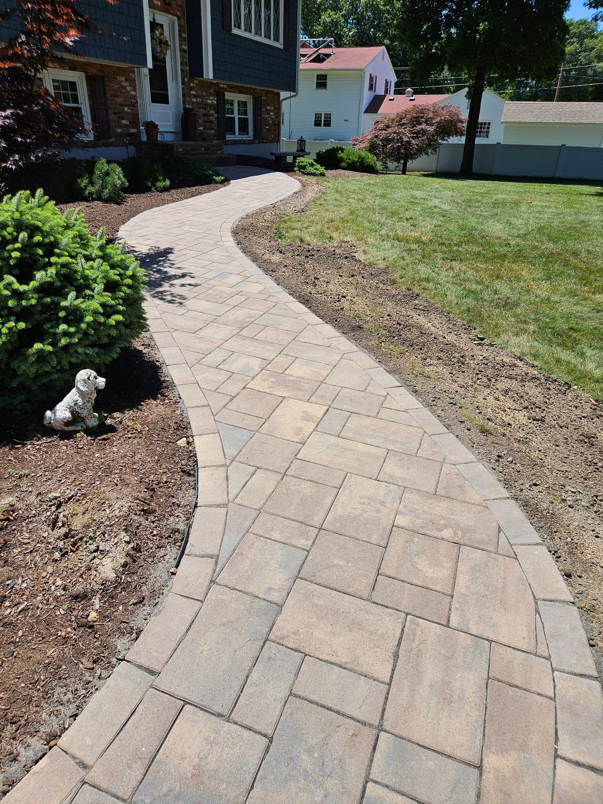 A dog is standing on a sidewalk next to a house.