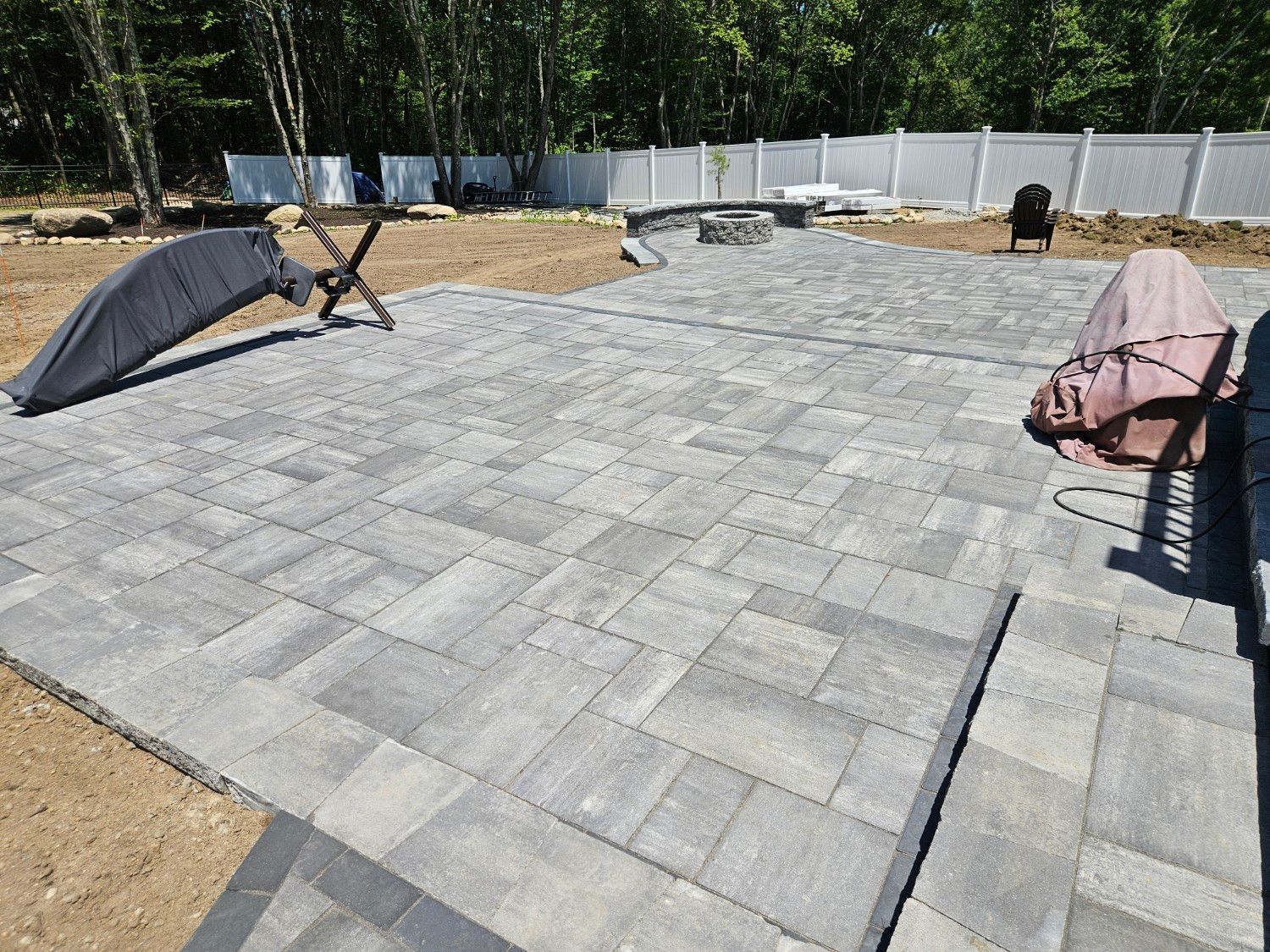 Patio with gray pavers, a fire pit, and two lounge chairs in a backyard area