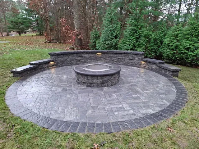 Stone patio fire pit with curved bench seating in a landscaped backyard