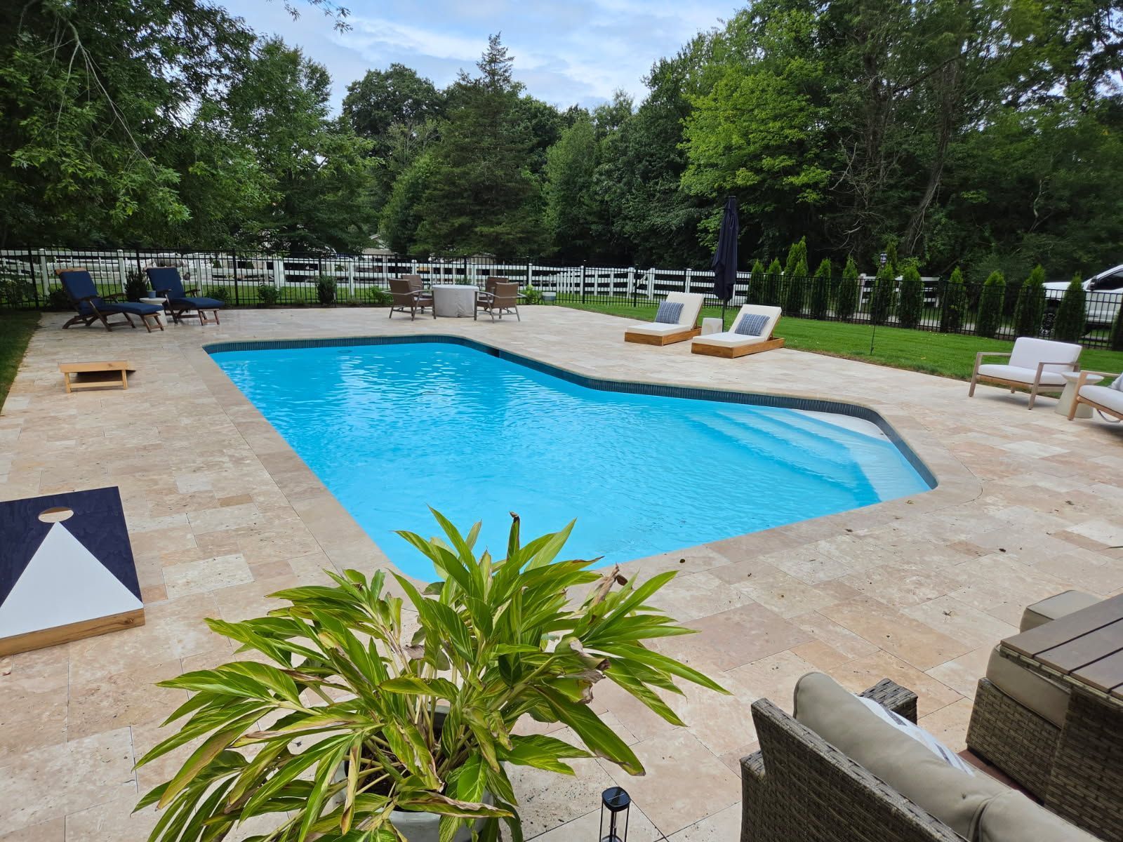 Backyard pool with turquoise water, lounge chairs, potted plants, and a stone patio surrounded by trees