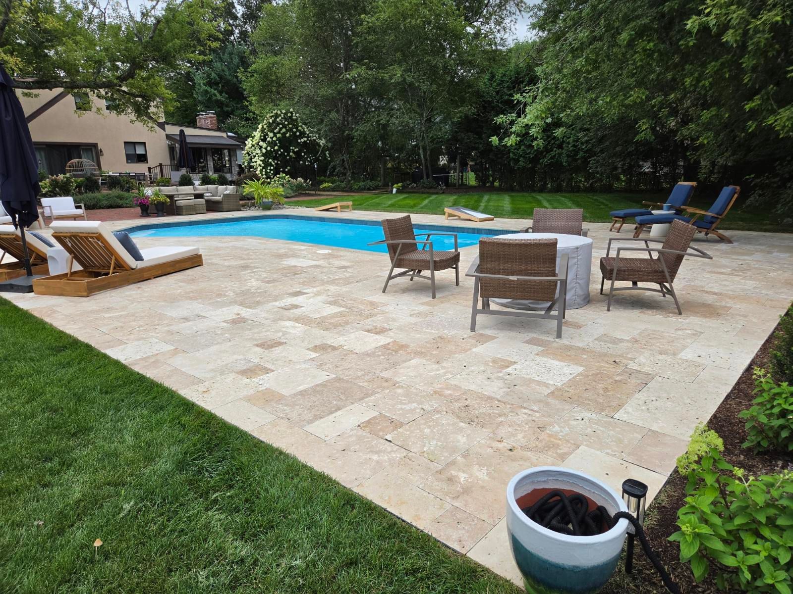Patio with a swimming pool, wicker chairs, and a potted plant in a backyard.