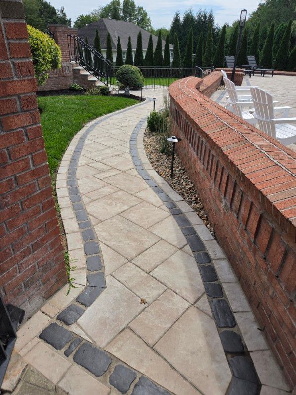 Curved brick-and-stone walkway beside a pool, with manicured lawn and landscaping in the background