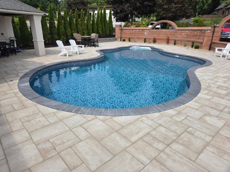Backyard pool with blue water, light stone patio, white lounge chairs, and brick wall seating area