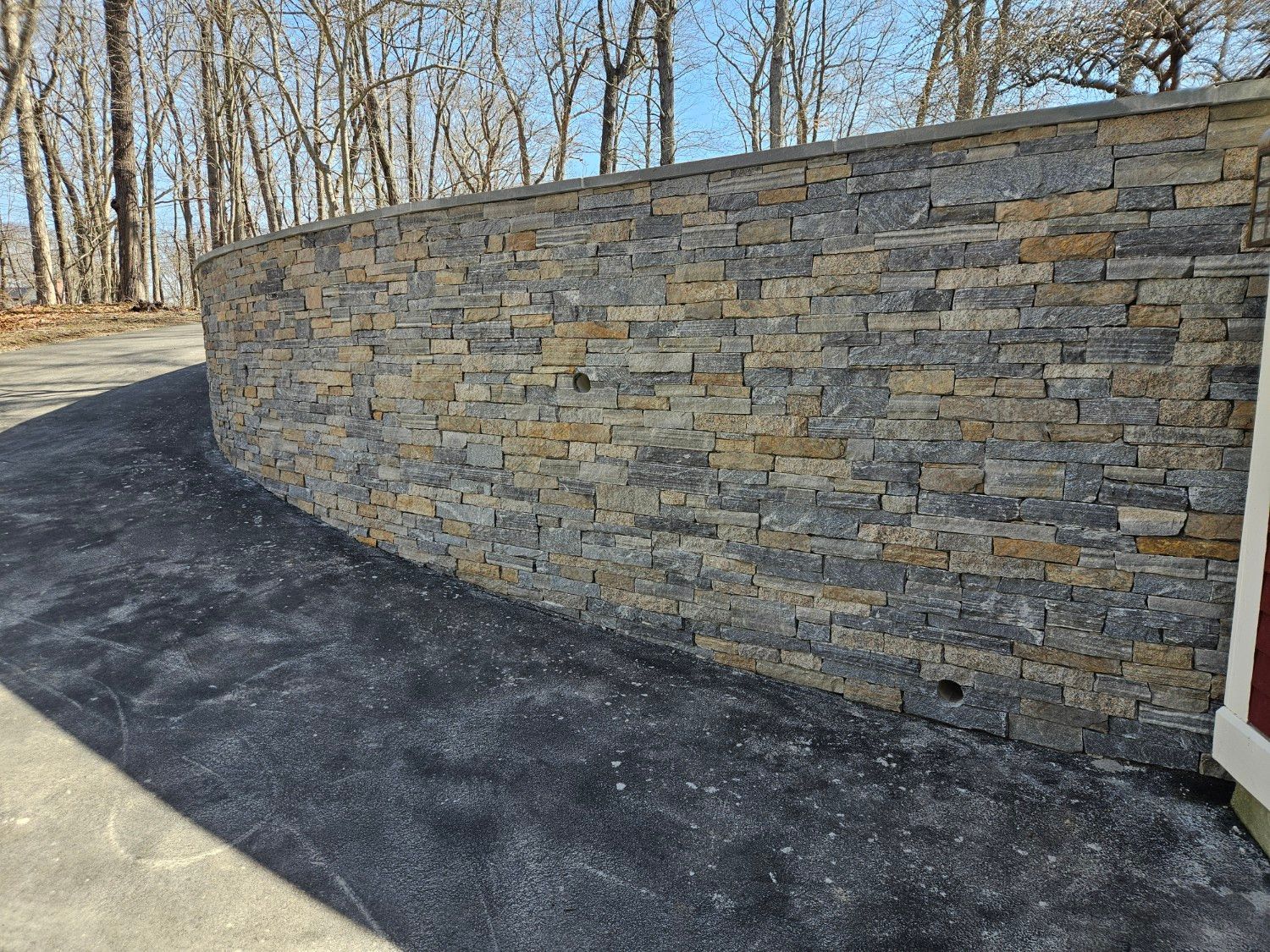 A stone wall surrounds a driveway with trees in the background.