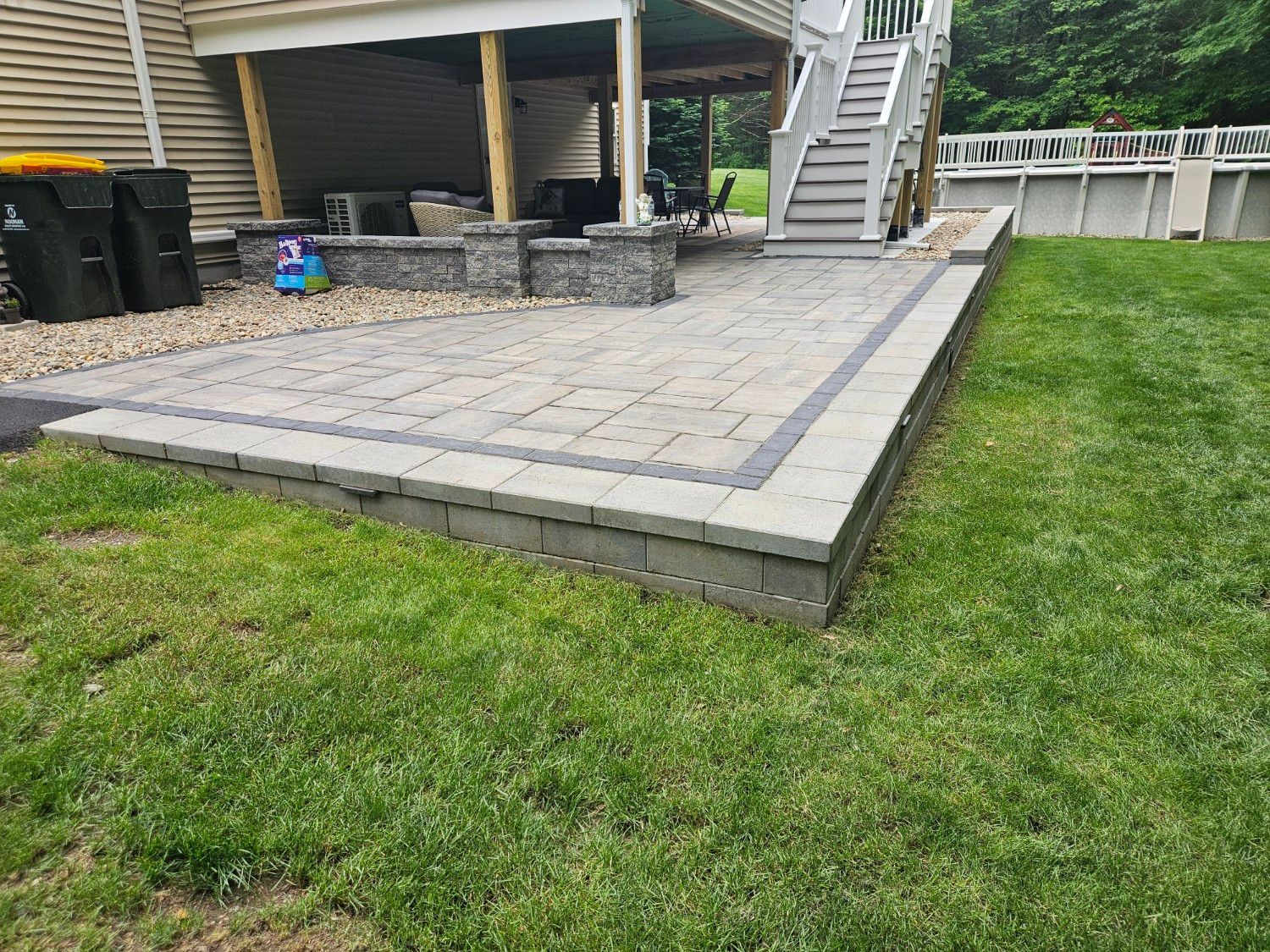 A patio with a staircase leading up to it is in the backyard of a house.