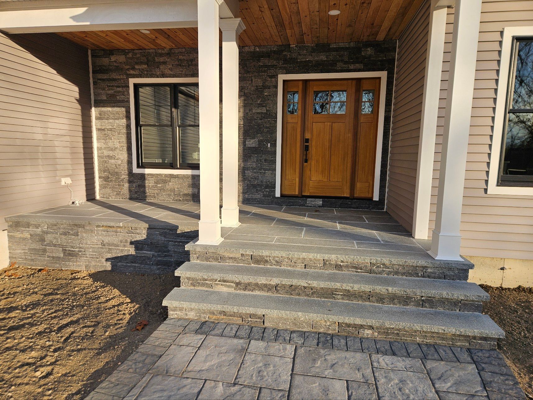 Front entrance with stone steps, wooden door, and pillars. Gray and brown tones.