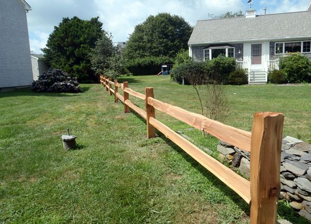 A wooden fence surrounds a lush green yard in front of a house.