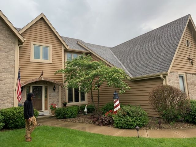 A man is standing in front of a large house with an american flag.