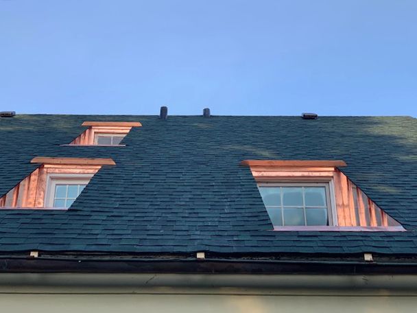 A roof with two windows on it and a blue sky in the background.