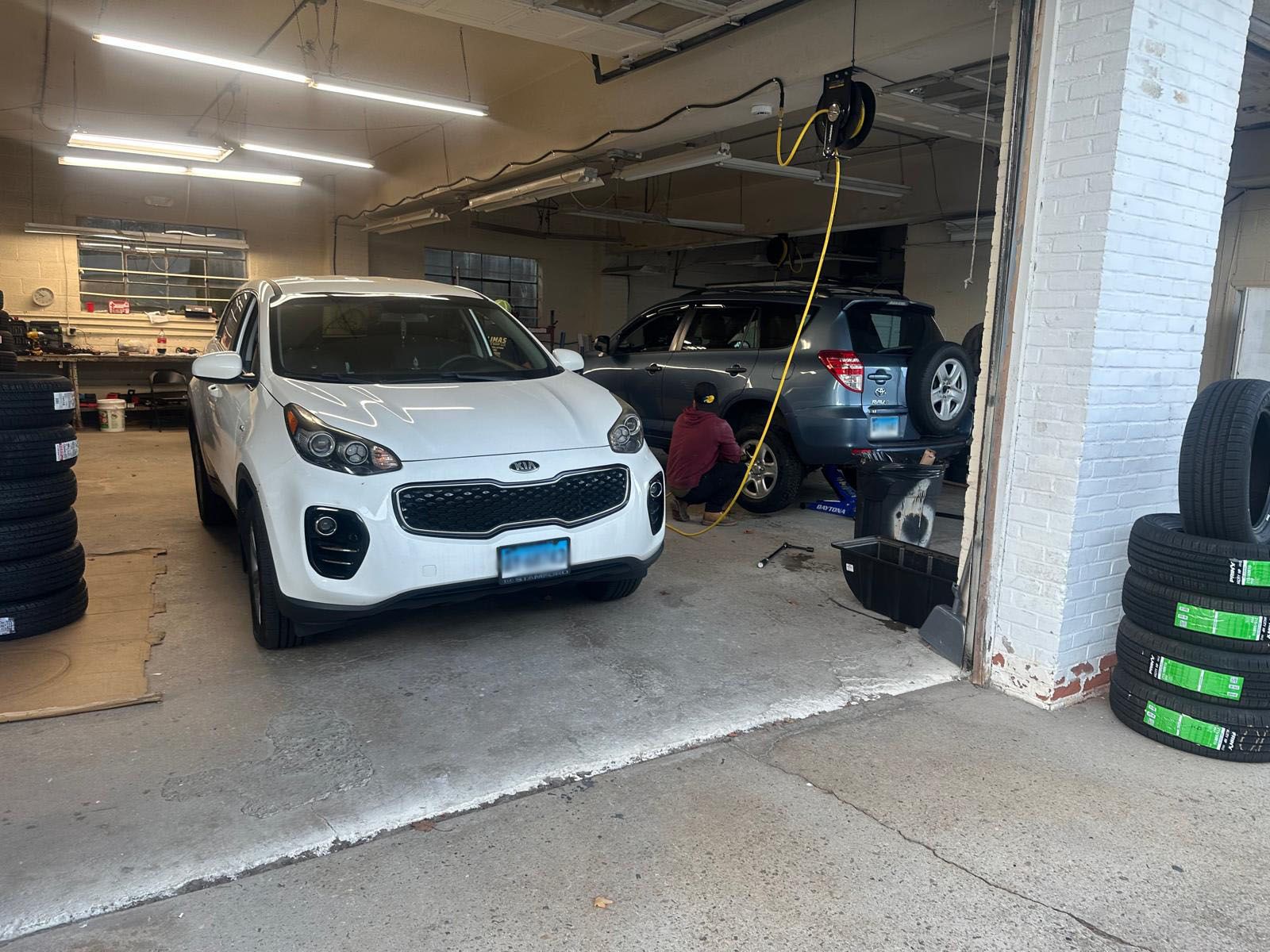 A white car is parked in a garage next to a stack of tires.