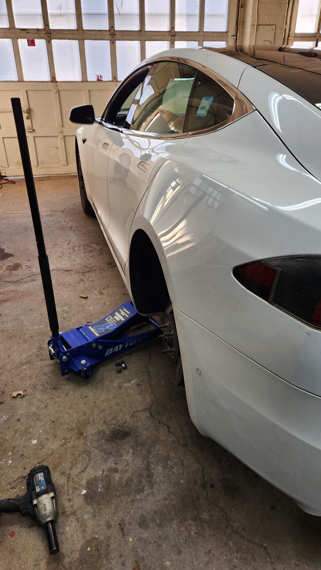 A white tesla model 3 is sitting on a jack in a garage.