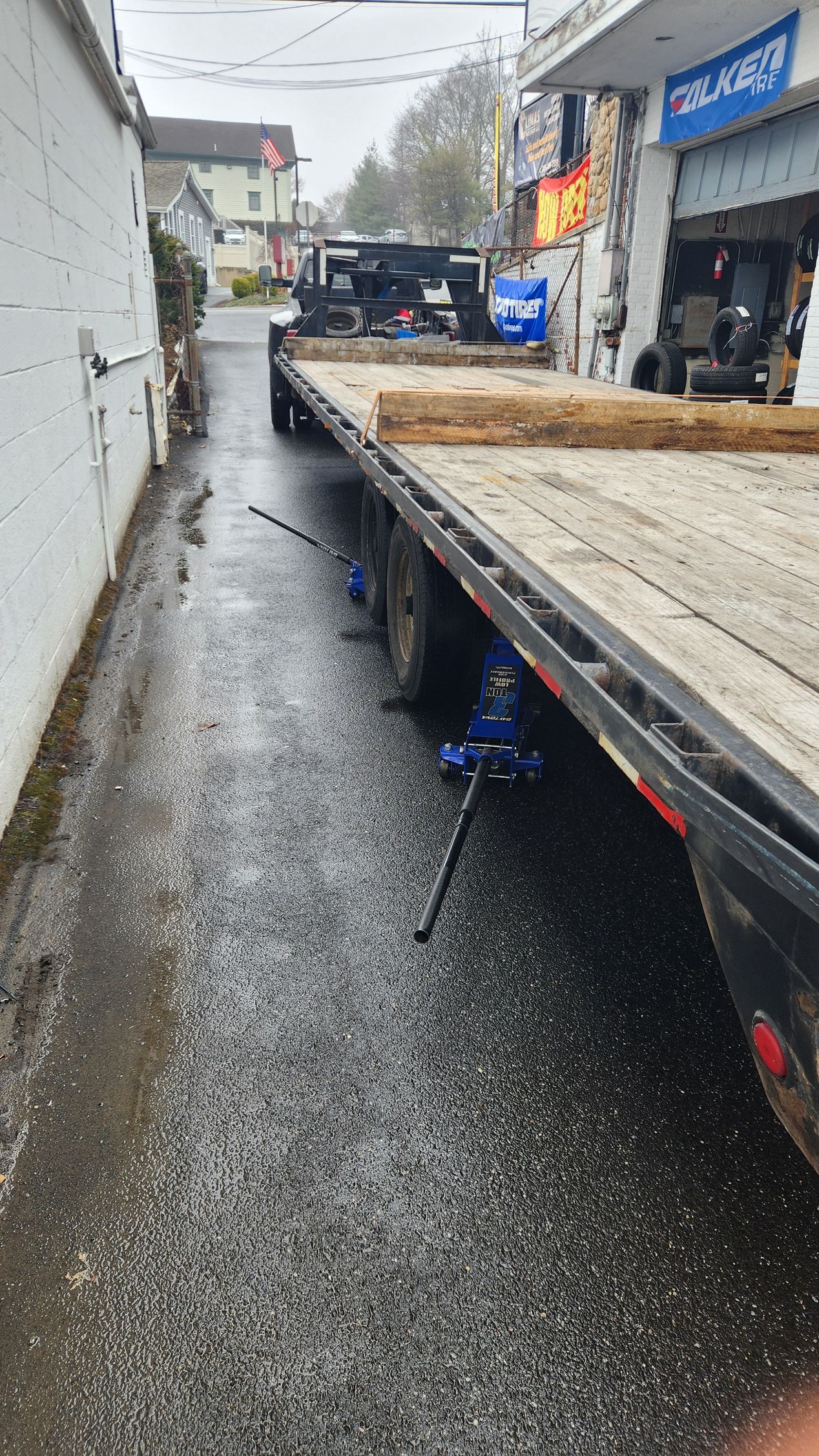 A flatbed tow truck is parked in a narrow alleyway next to a building.