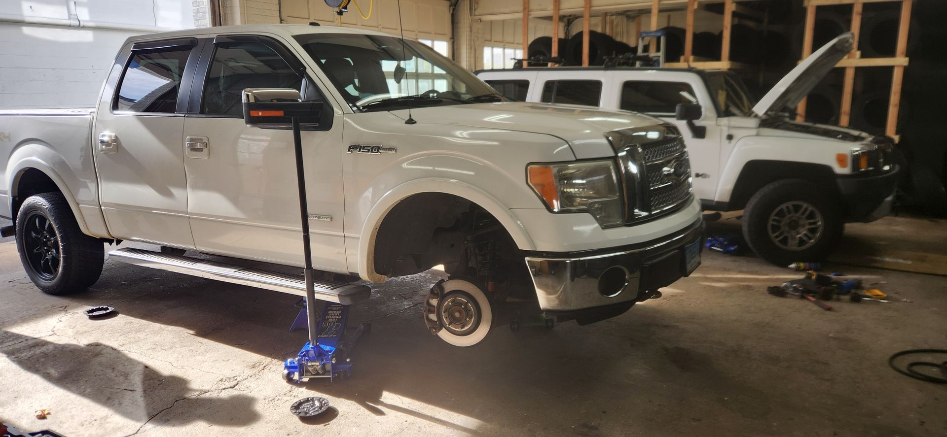 A white truck is sitting on a jack in a garage.