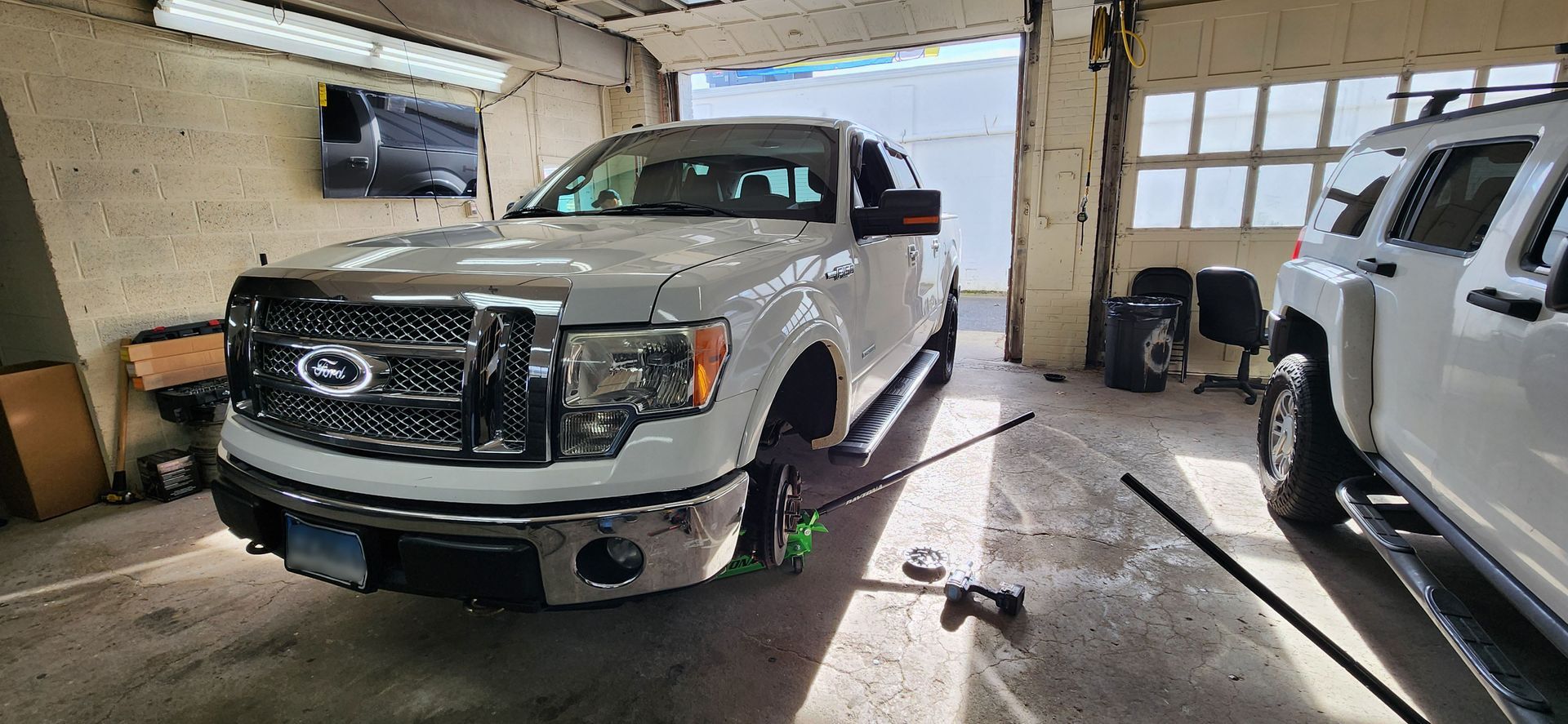 A white truck is parked in a garage next to another truck.