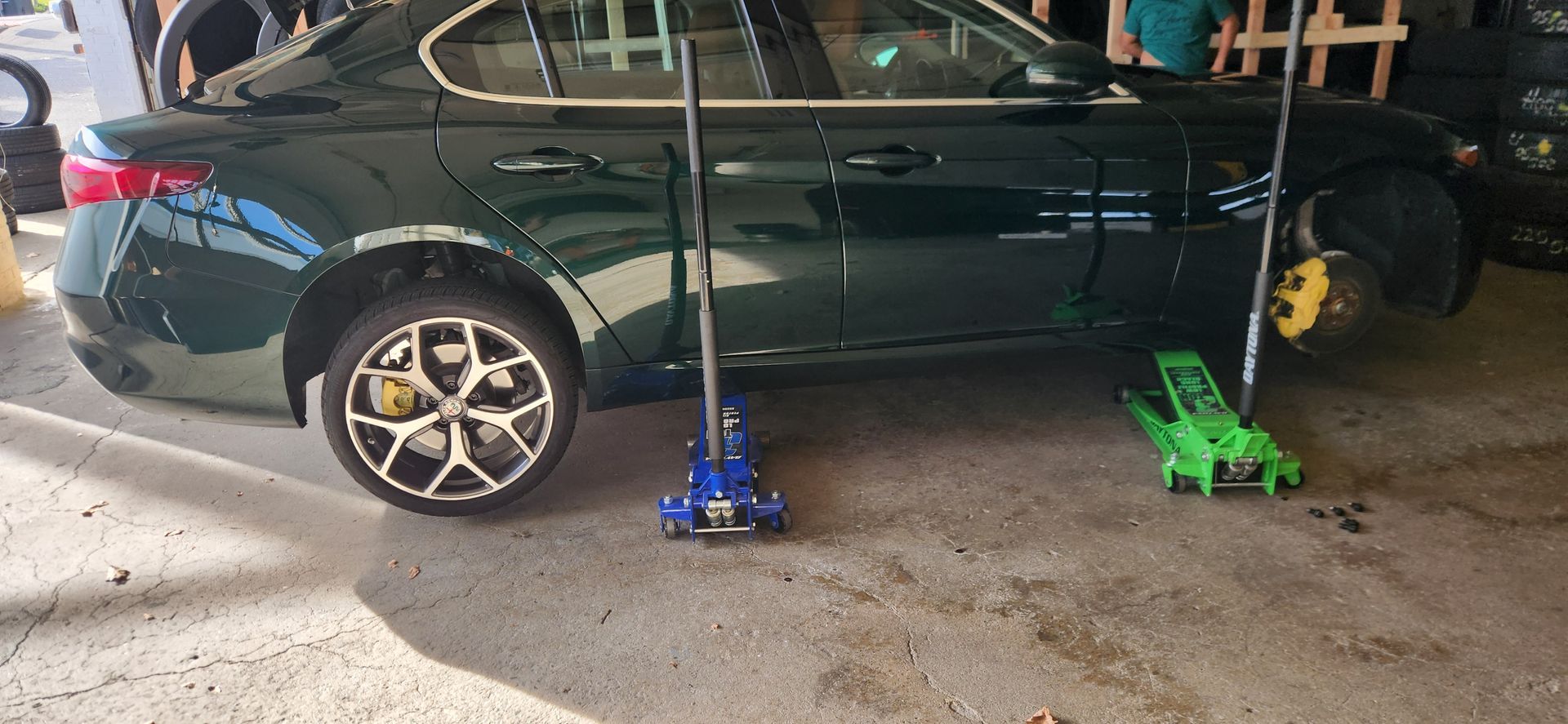 A green car is sitting on a jack in a garage.