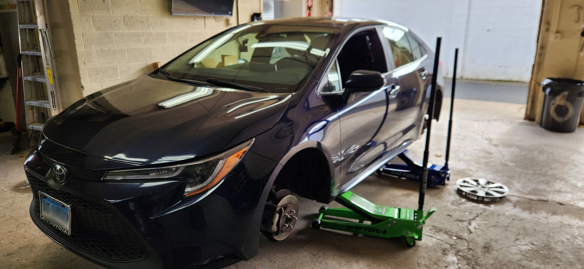A black car is sitting on a green jack in a garage.