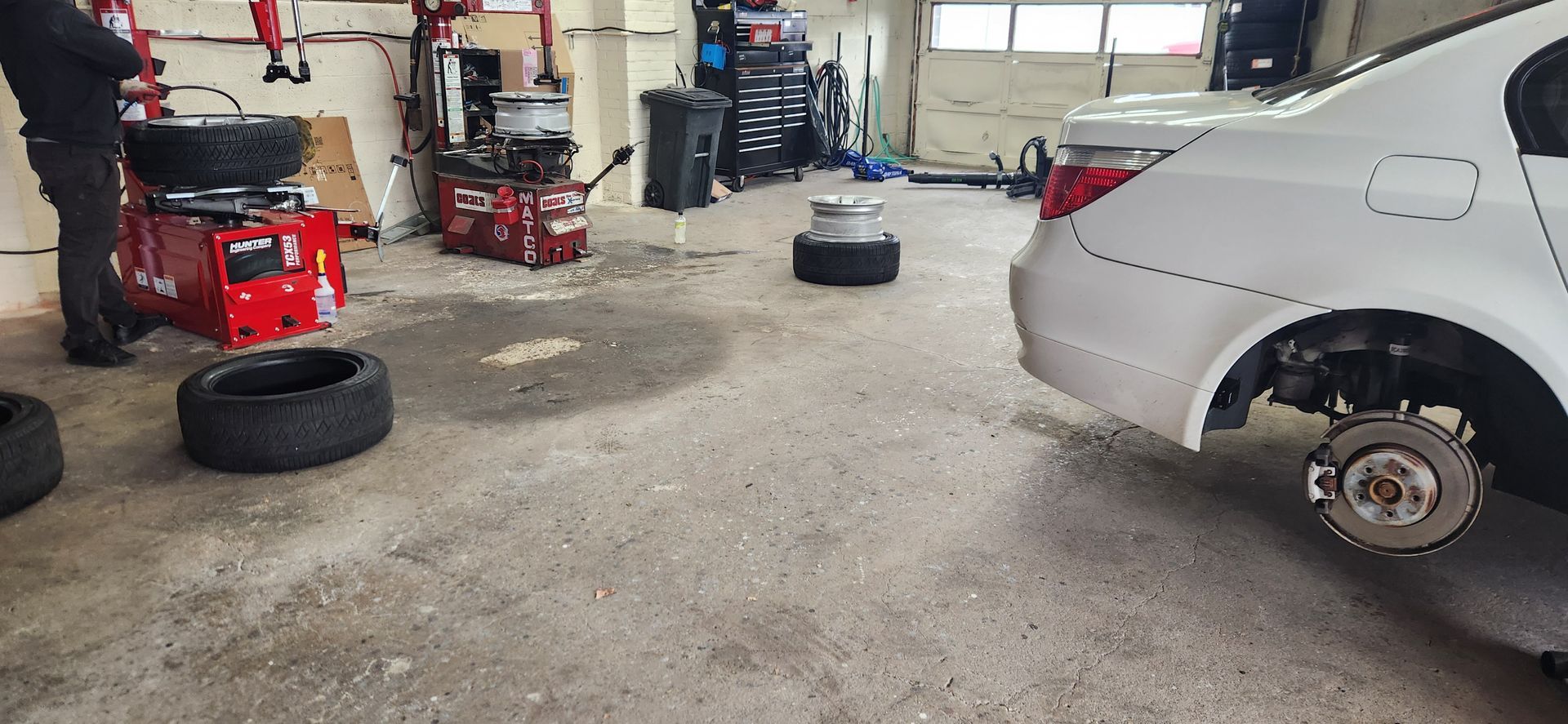 A man is changing a tire on a white car in a garage.