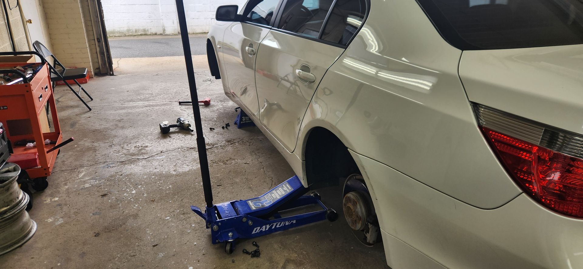 A white car is sitting on a blue jack in a garage.