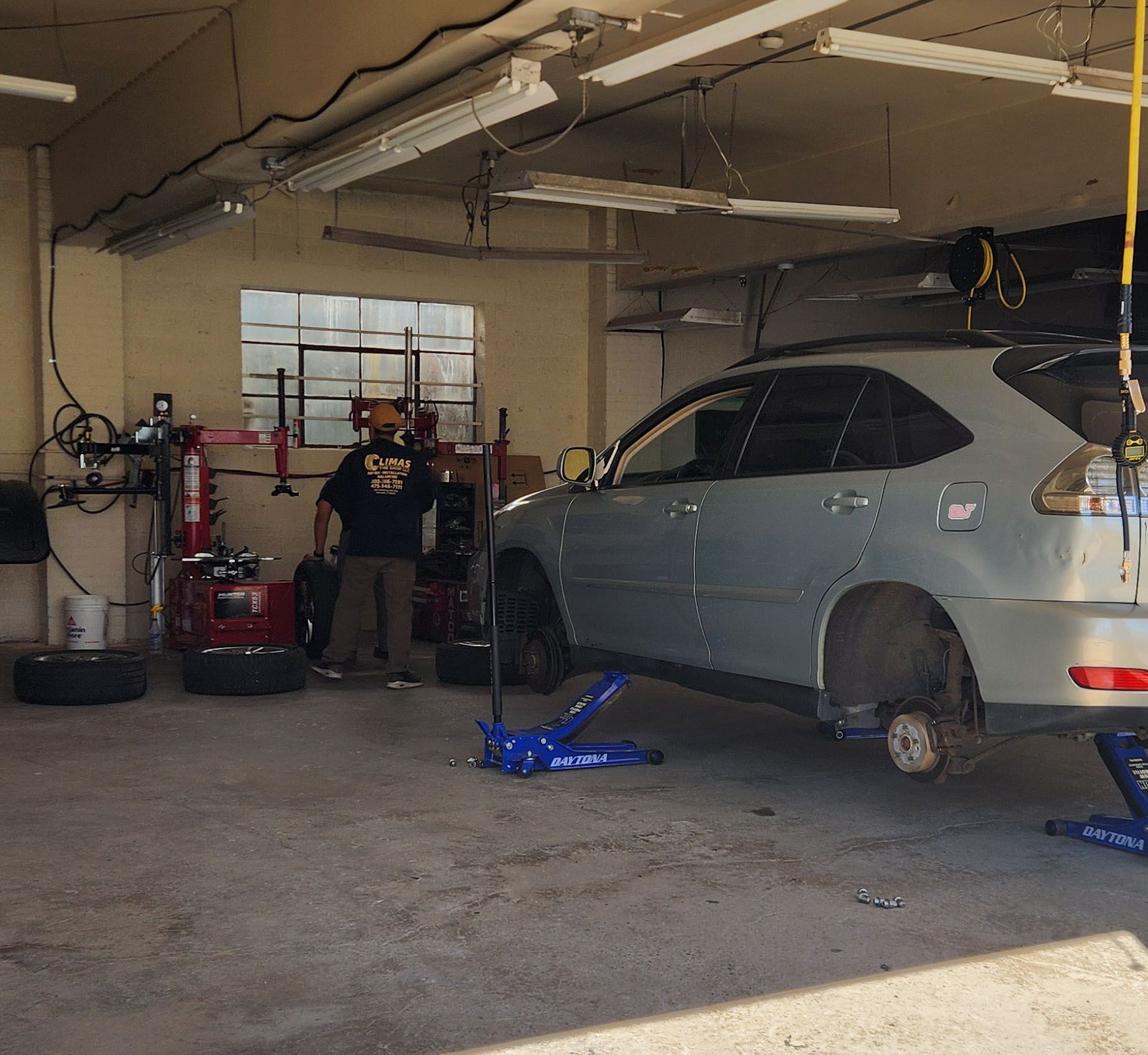 A man wearing a shirt that says ' a ' on it stands next to a car in a garage
