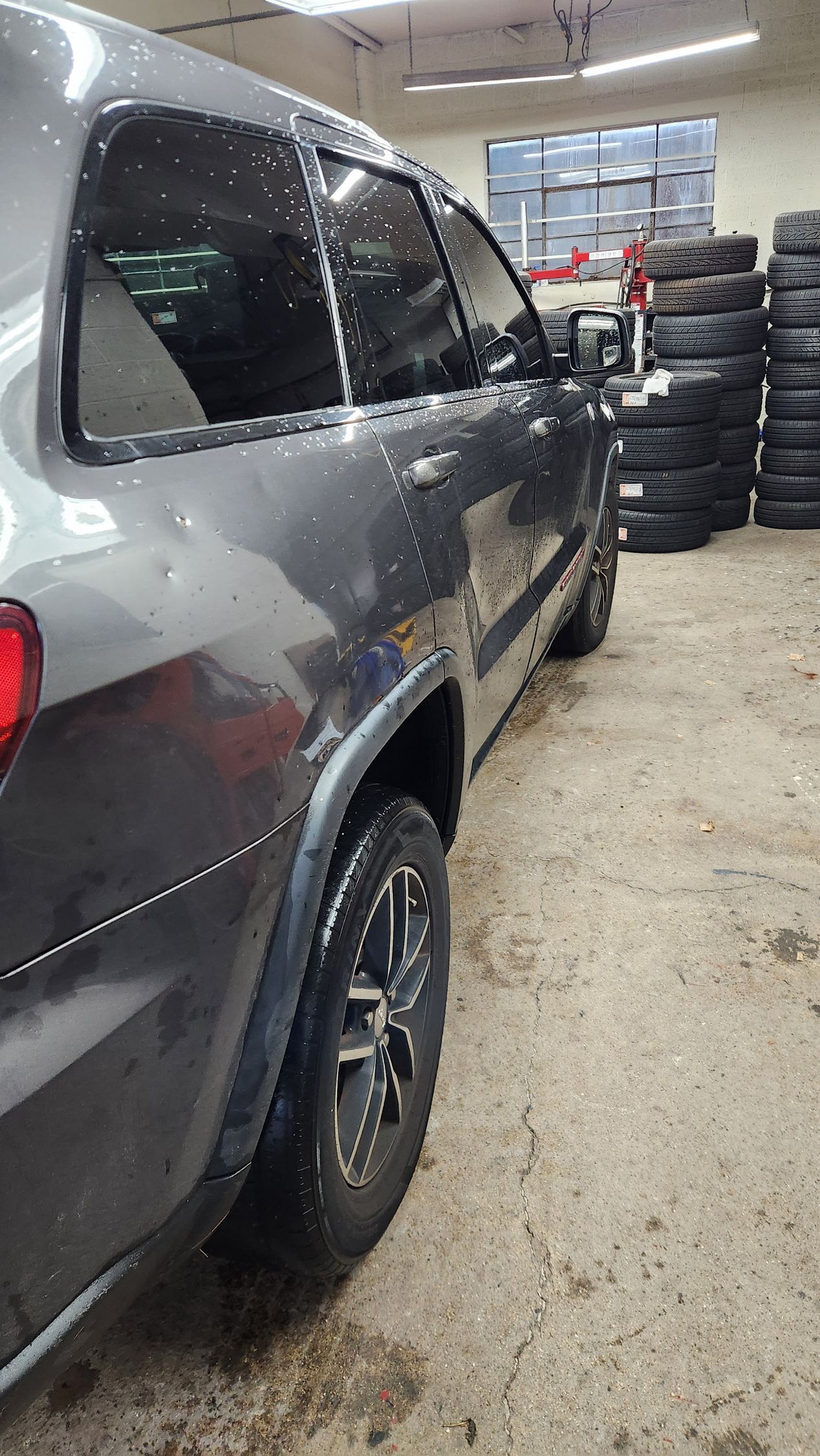 A jeep grand cherokee is parked in a garage next to a pile of tires.