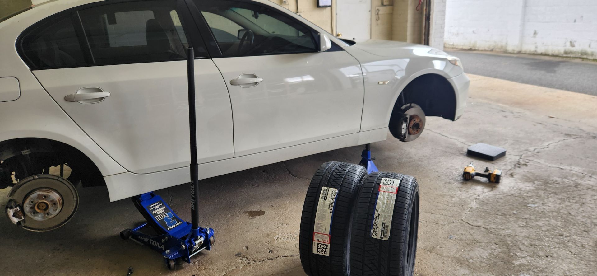 A white car is sitting on a jack next to two tires.