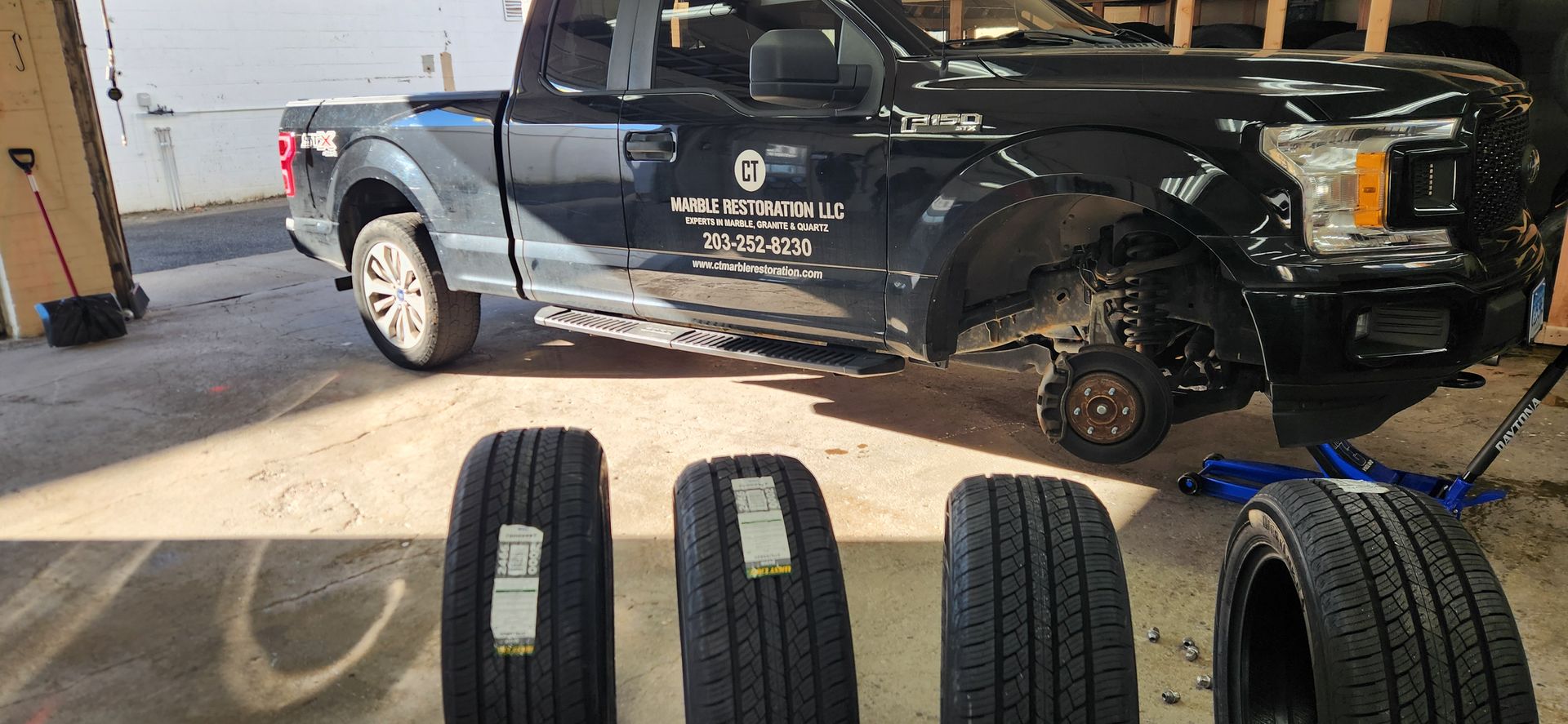 A black truck is parked in a garage next to three tires.