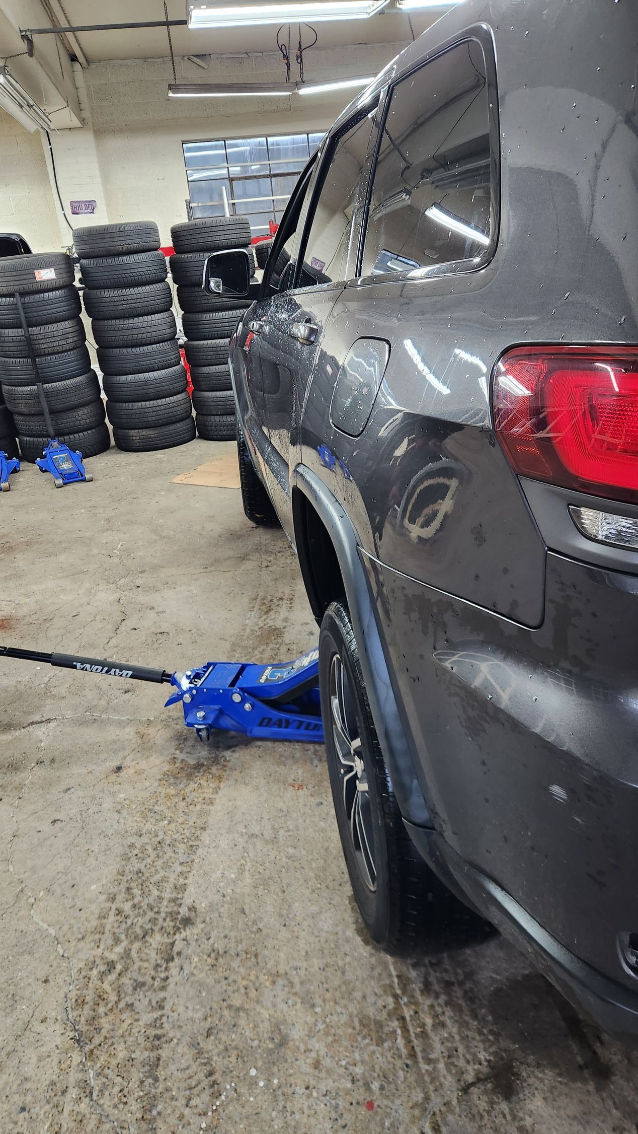 A car is sitting on a jack in a garage next to a pile of tires.