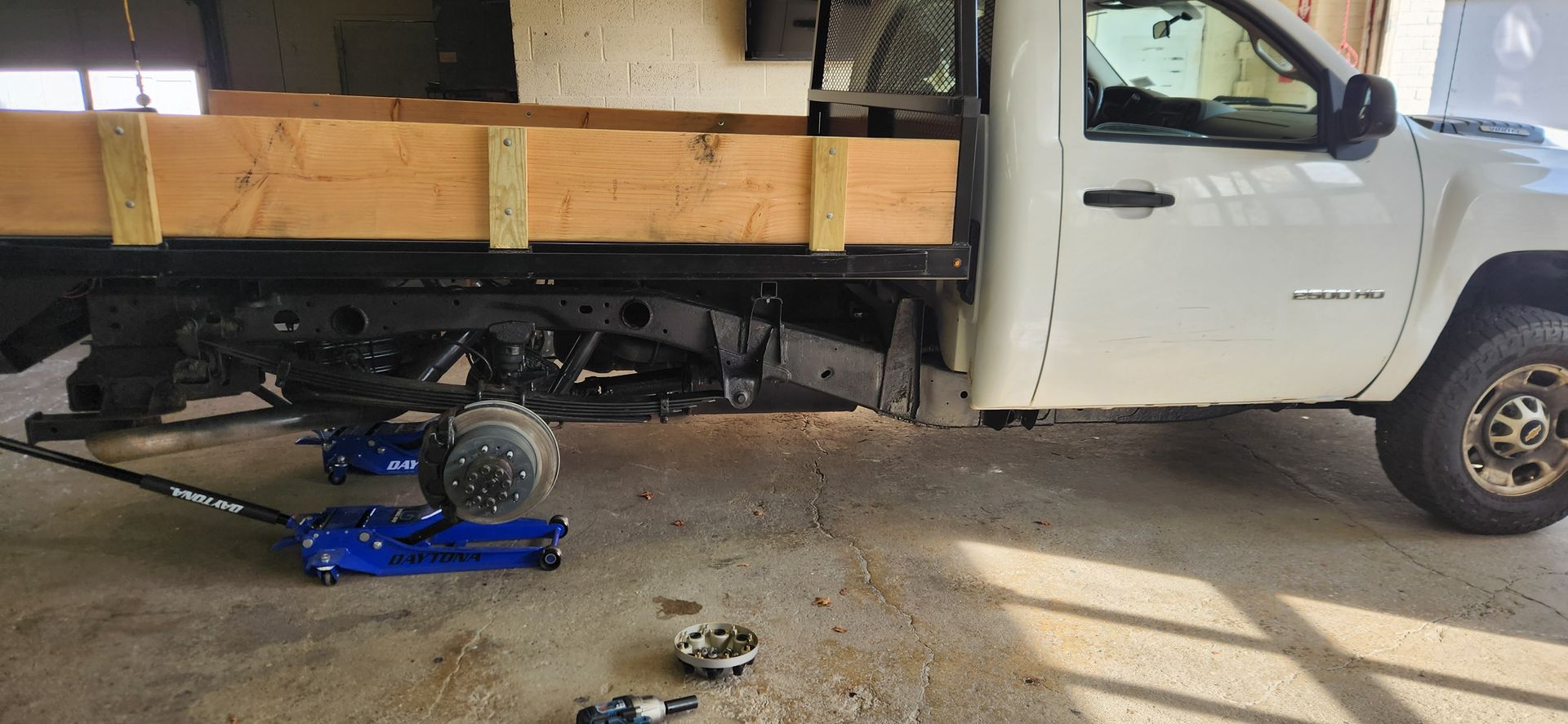 A white truck is sitting on a jack in a garage.