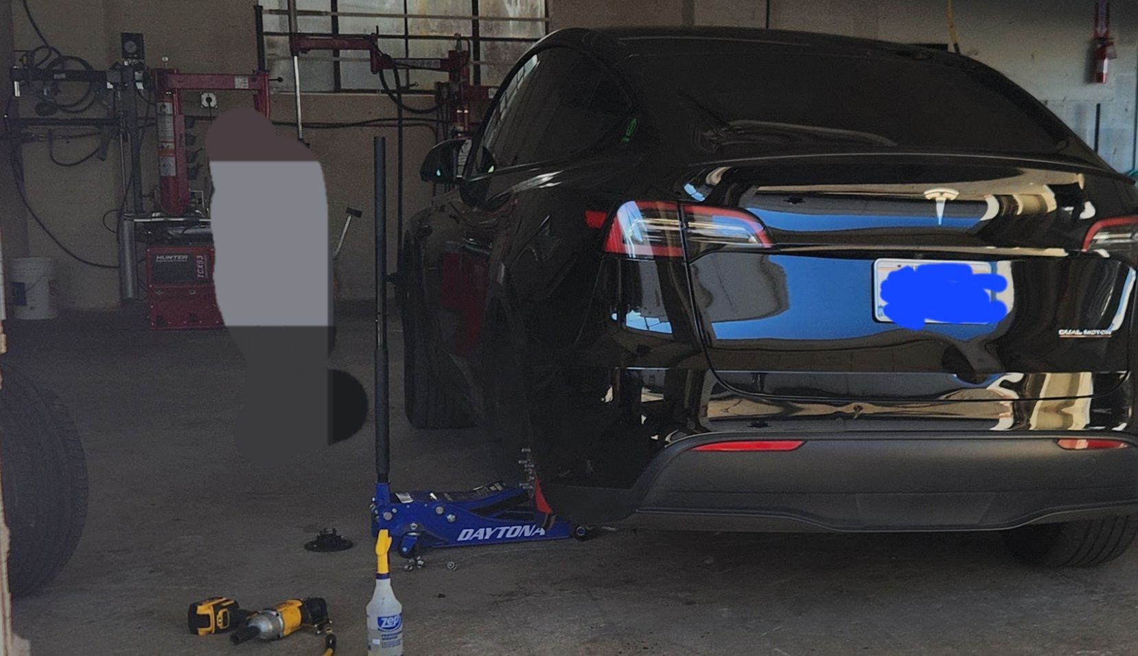 A black car is parked in a garage with a blue license plate.