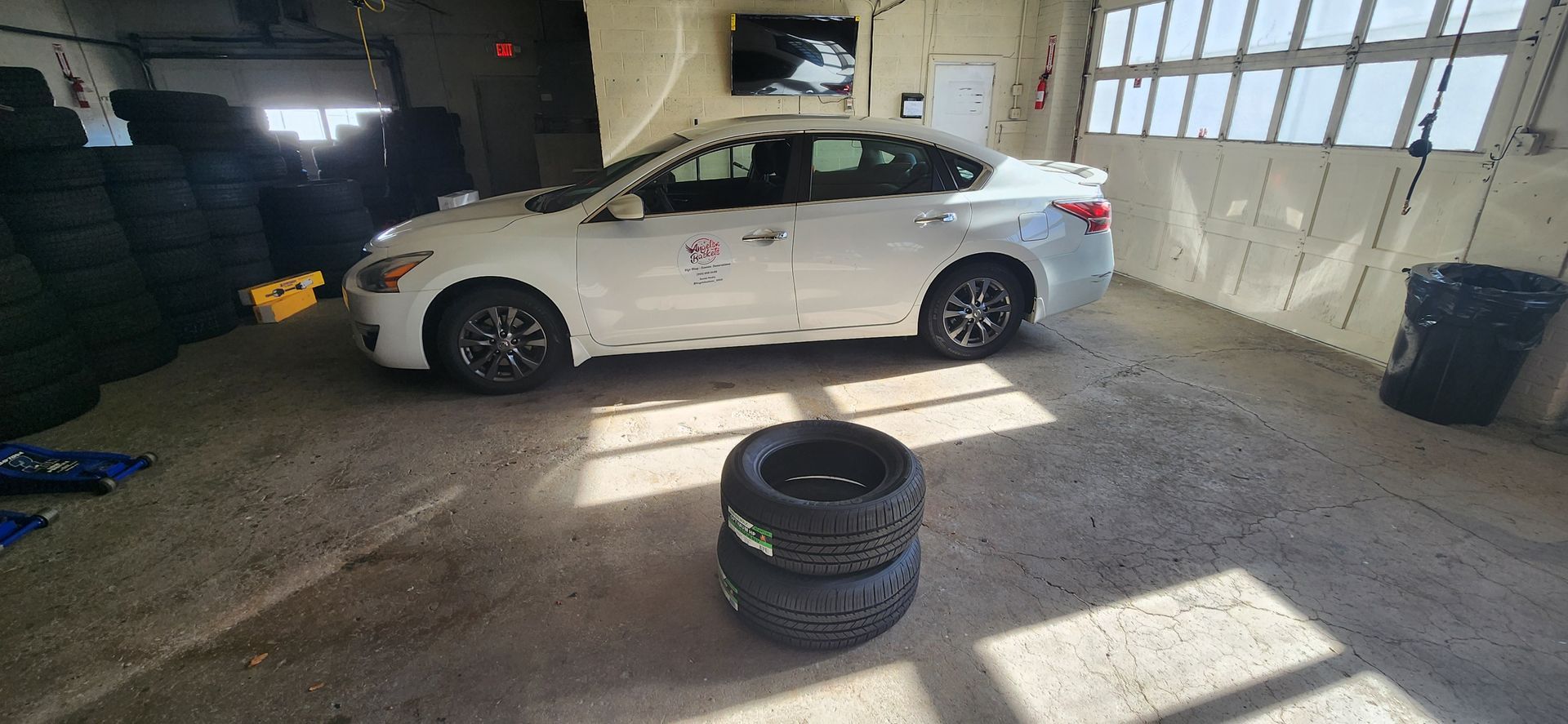 A white car is parked in a garage next to two tires.