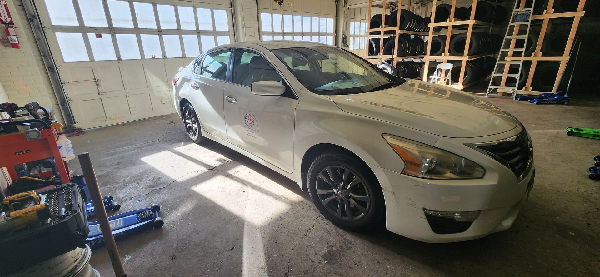 A white car is parked in a garage next to a tire rack.