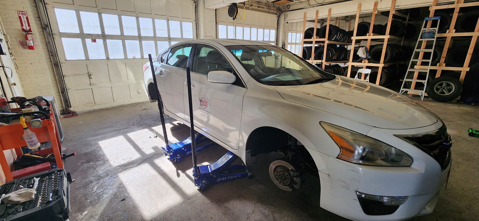 A white car is sitting on a jack in a garage.