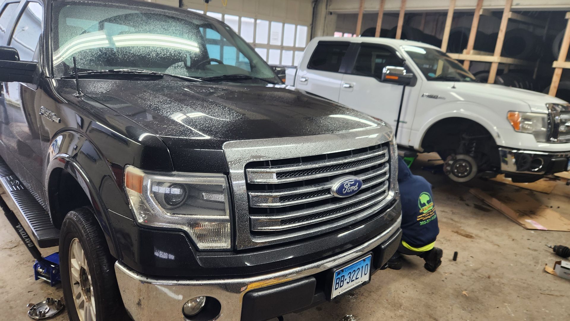 A black ford truck is parked next to a white truck in a garage.