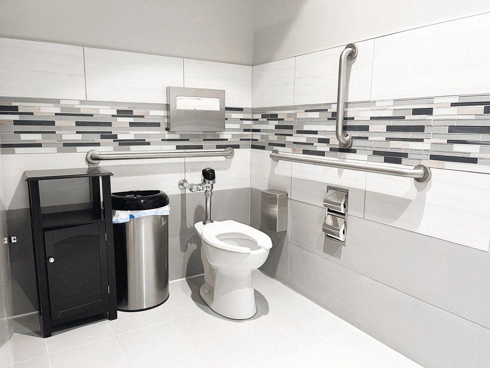 A bathroom with a toilet , trash can , and handrails.