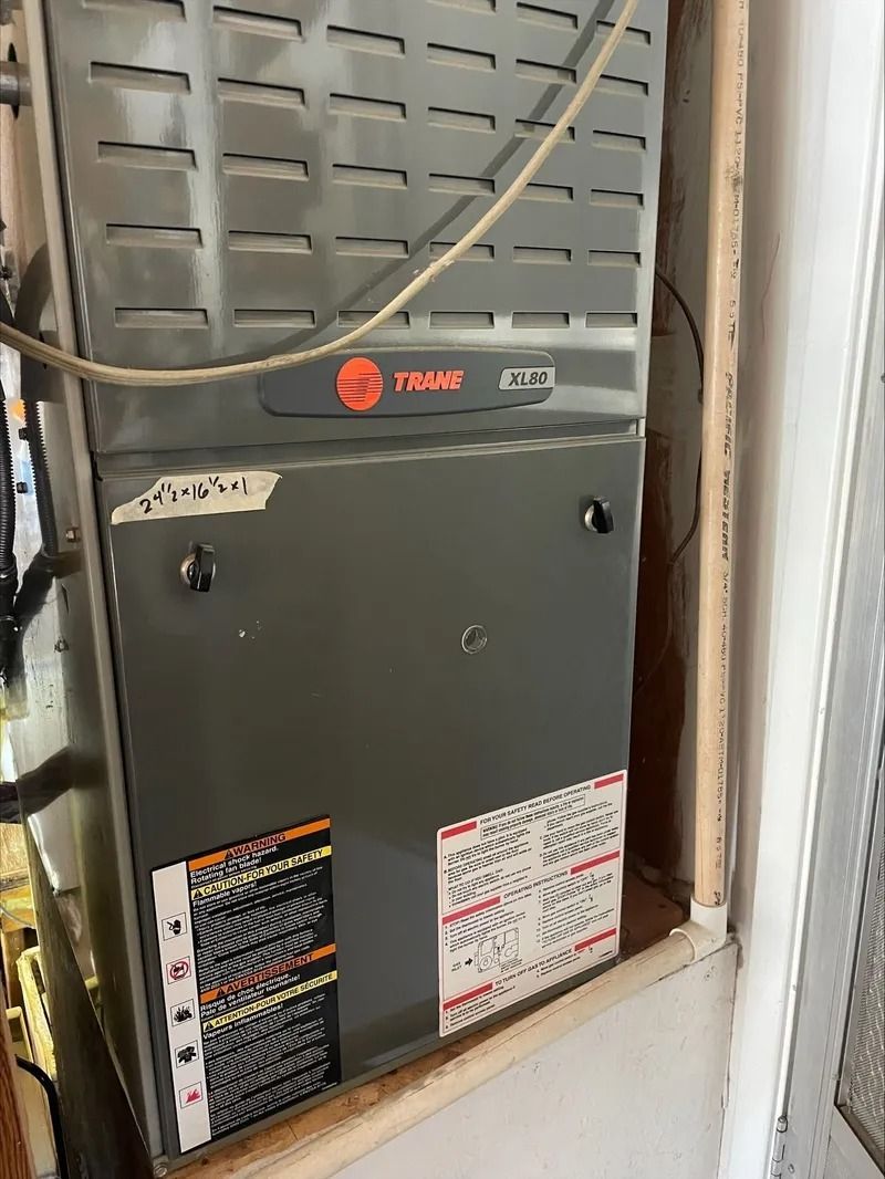A grey Trane furnace unit installed in a utility closet with a wiring diagram label on the front panel.